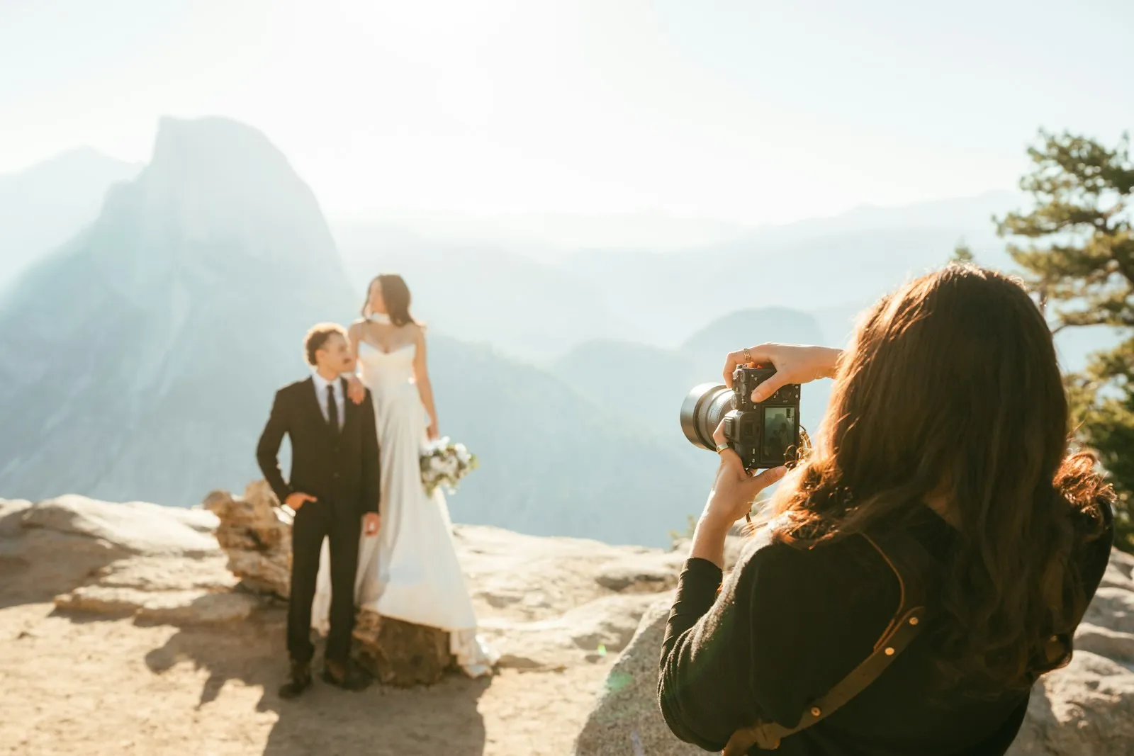 A photographer, seen from behind, photographs a couple on a mountain overlook